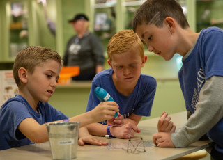 Three boys use a 3D printing pen to create a small art piece.
