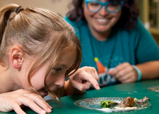 young girl pointing at snails and a teacher smiling in the background